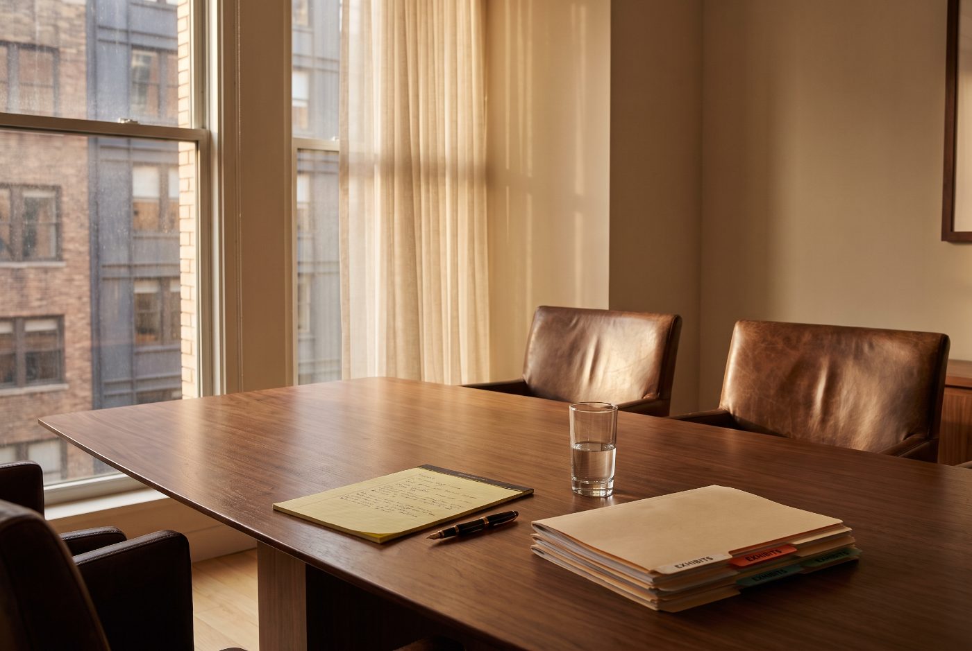 Corner of a law office conference room with leather chairs, a legal pad and a stack of tabbed exhibit binders on a polished table